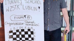2 bibliotekarzy trzymających tablicę z napisem pierwszy turniej szachów w ZSTK Lublin.