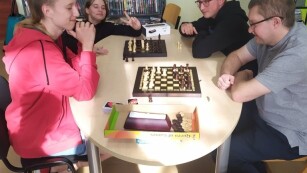 Trójka uczniów i nauczyciel grających w szachy przy stole bibliotece.
