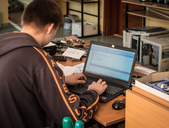 Uczeń siedzący przed laptopem, piszący kod w języku programowania
