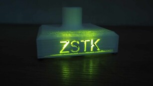 Podstawa choinki wykonana w technologii druku 3D, ze świecącym na zielono napisem ZSTK.