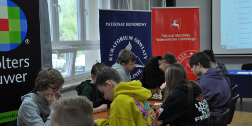 Uczestnicy w skupieniu siedzą przy szachownicach