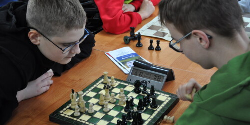 Uczestnicy w skupieniu siedzą przy szachownicach
